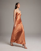 Model wearing a liquid silk slipdress in terracotta color, showcasing its elegant drape.