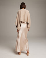 Model wearing a beige bolero over a satin slip dress, facing away from the camera.