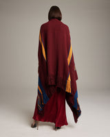 Model wearing a Cascade Wrap in Baby Alpaca, showcasing the back view with burgundy, orange, and blue colors.