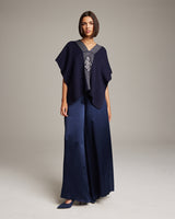 Model wearing a navy poncho with a geometric design and wide-leg pants.