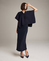 Model wearing a navy poncho with Araña symbol, standing in a studio setting.