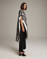 Model wearing a black and ivory poncho with geometric patterns, showcasing the Manta Comunidad design.