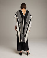 Model wearing a black and ivory poncho with geometric patterns, viewed from the back