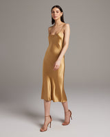 Model wearing a gold midi slip dress with spaghetti straps