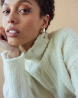 Model wearing a ribbed cropped sweater with a high neck and earrings, close-up shot