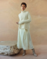 Model wearing an oversized ribbed knit sweater with a side slit and a panelled wrap skirt in ivory.