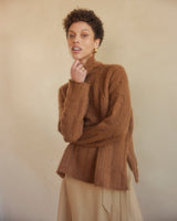 Model wearing an oversized ribbed knit sweater in camel color, posing with a thoughtful expression.
