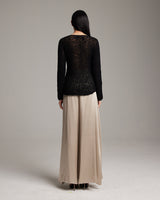 Model wearing a black sweater and beige silk palazzo pants from the back