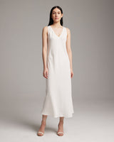 Model wearing a white linen V neck dress, standing on a neutral background.