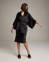 Model wearing a black silk kimono with a matching belt, styled with a dress and heels.