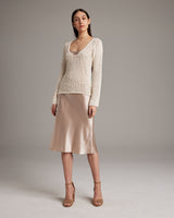 Model wearing a Flammé Loose Knit Long Sweater in ivory, paired with a satin skirt.