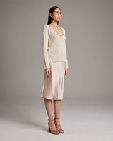 Model wearing a Flammé Loose Knit Long Sweater in ivory, paired with a satin skirt.