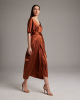 Model wearing a rust-colored kaftan dress with a belt, showcasing its elegant drape.