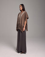 Model wearing a brown Lineas Fringe Manta poncho with fringes, styled with a long skirt.