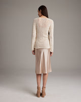 Back view of a model wearing a cream Flammé Loose Knit Long Sweater with a satin skirt