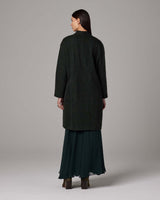Back view of a model wearing a handwoven alpaca Lineas coat in forest color