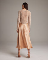 Back view of a model wearing a painted loose knit cropped sweater with a satin skirt