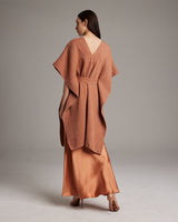 Model wearing a shimmering copper kaftan with a flowing design, paired with a satin slipdress.