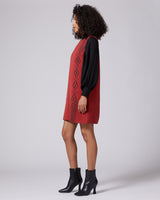 Model wearing a sleeveless red dress with black sleeves and diamond patterns, side view