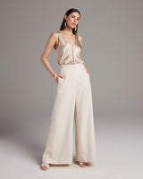 Model wearing high waist wide trousers in pearl color, showcasing pockets and a stylish look.