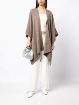 Model wearing a brown Raíz Duster over a white outfit, holding a silver bag.
