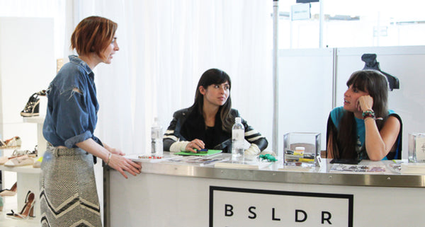 Three women at a fashion event, one speaking while the others listen.
