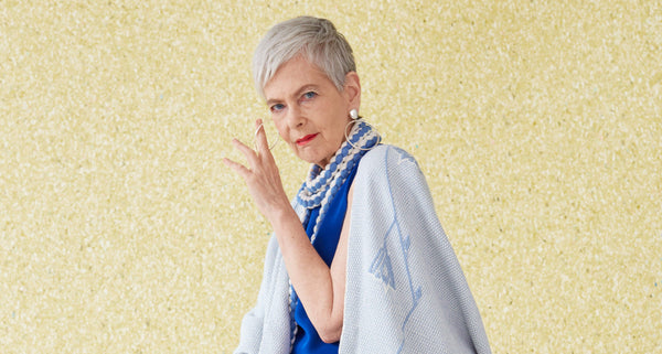 Lyn Slater posing with a blue outfit and jewelry against a gold background
