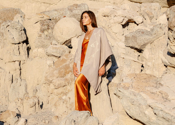 A woman in a beige shawl and orange dress standing on rocky terrain