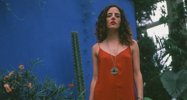 Daniela Perdomo standing in front of a blue wall with plants, wearing a red dress and necklace