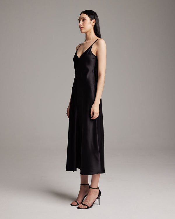 Model wearing a black V-neck slip dress with spaghetti straps, standing sideways.