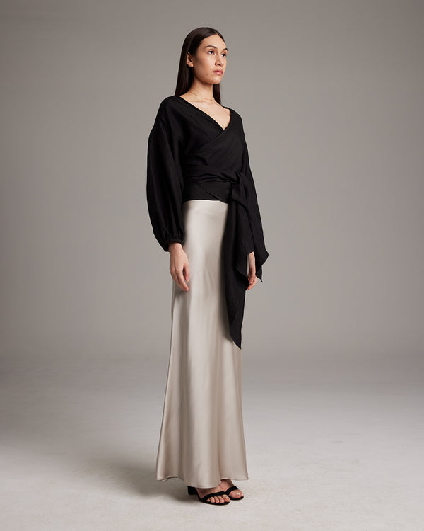 Model wearing a black peasant wrap blouse with a beige skirt