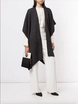 Model wearing a solid merino duster over a white outfit, holding a black bag.