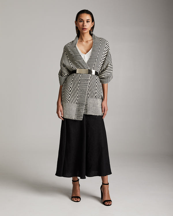 Model wearing a Chevron Shawl in Baby Alpaca with a belt, showcasing a black skirt and high heels.