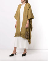Model wearing a curvy fringe duster in a light brown color, with fringe edges, paired with a white dress and black shoes.