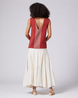 Model wearing a brick-colored Estrella V-Back Top with a v-back detail, paired with a white skirt.