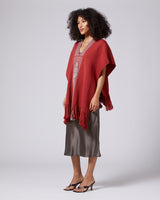 Model wearing a brick-colored poncho with fringe, featuring the Estrella symbol.