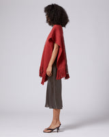 Side view of a woman wearing a brick-colored poncho with fringe, showcasing the Manta Araña design.