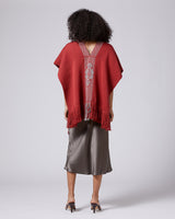 Model wearing a red Manta Araña poncho with fringe, showing back view