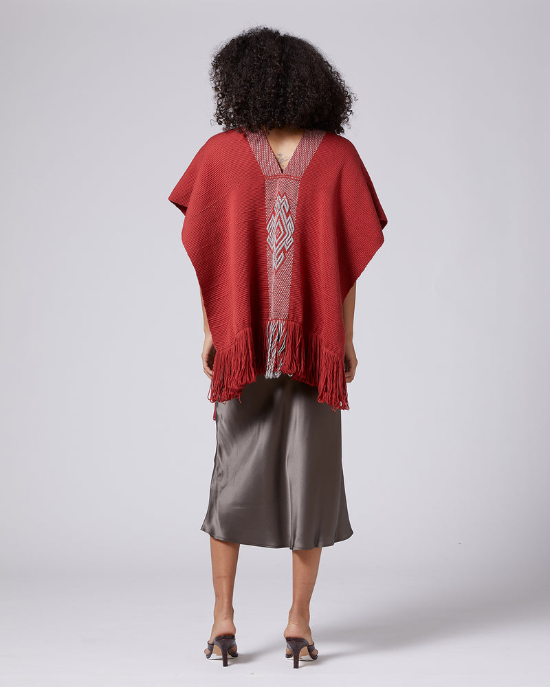 Model wearing a red Manta Araña poncho with fringe, showing back view
