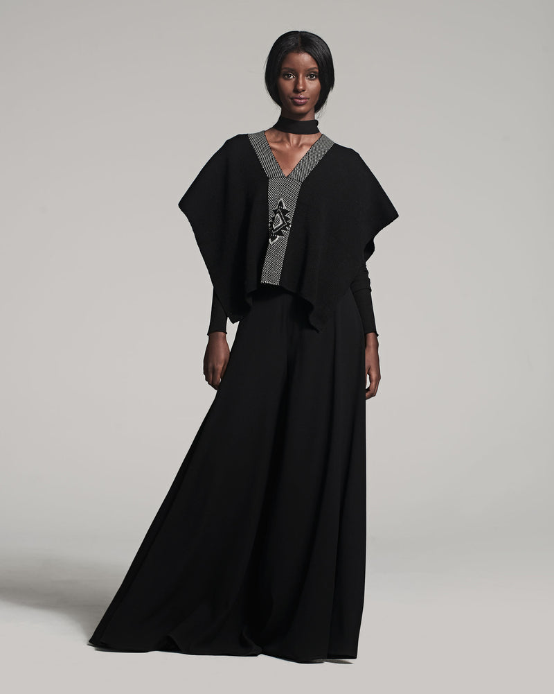 Model wearing a black poncho with a decorative neckline and a long black skirt